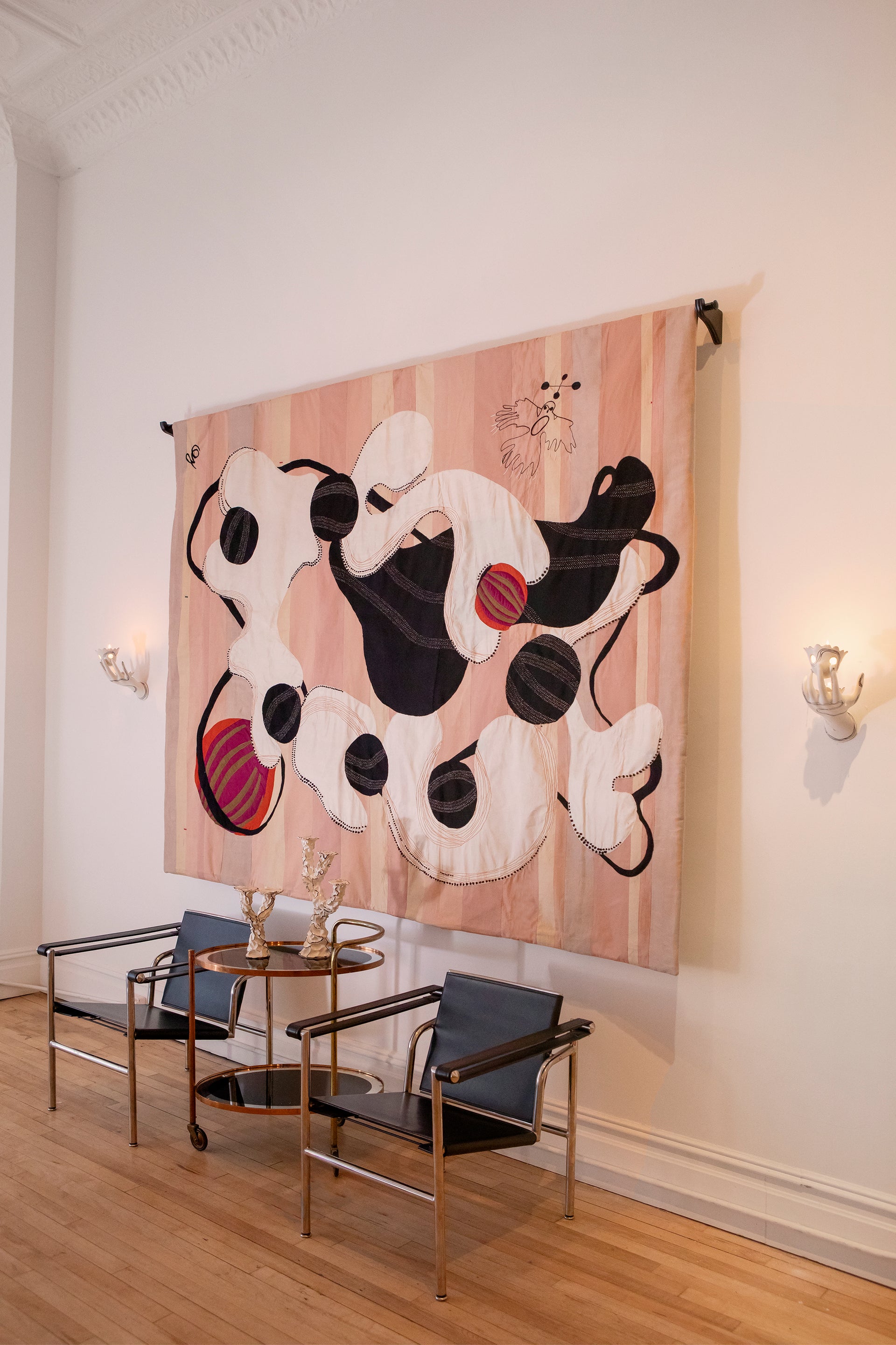 Hand made decorative tapestry with an abstract and surrealist design motif. White and black abstract shapes float on a pink background with an embroidered bird. Hand crafted and hand embroidered from antique silks. Made in India, artisanal home decor. Modern tapestry design. Shown in a home setting with other modernist home decor and furniture. 
