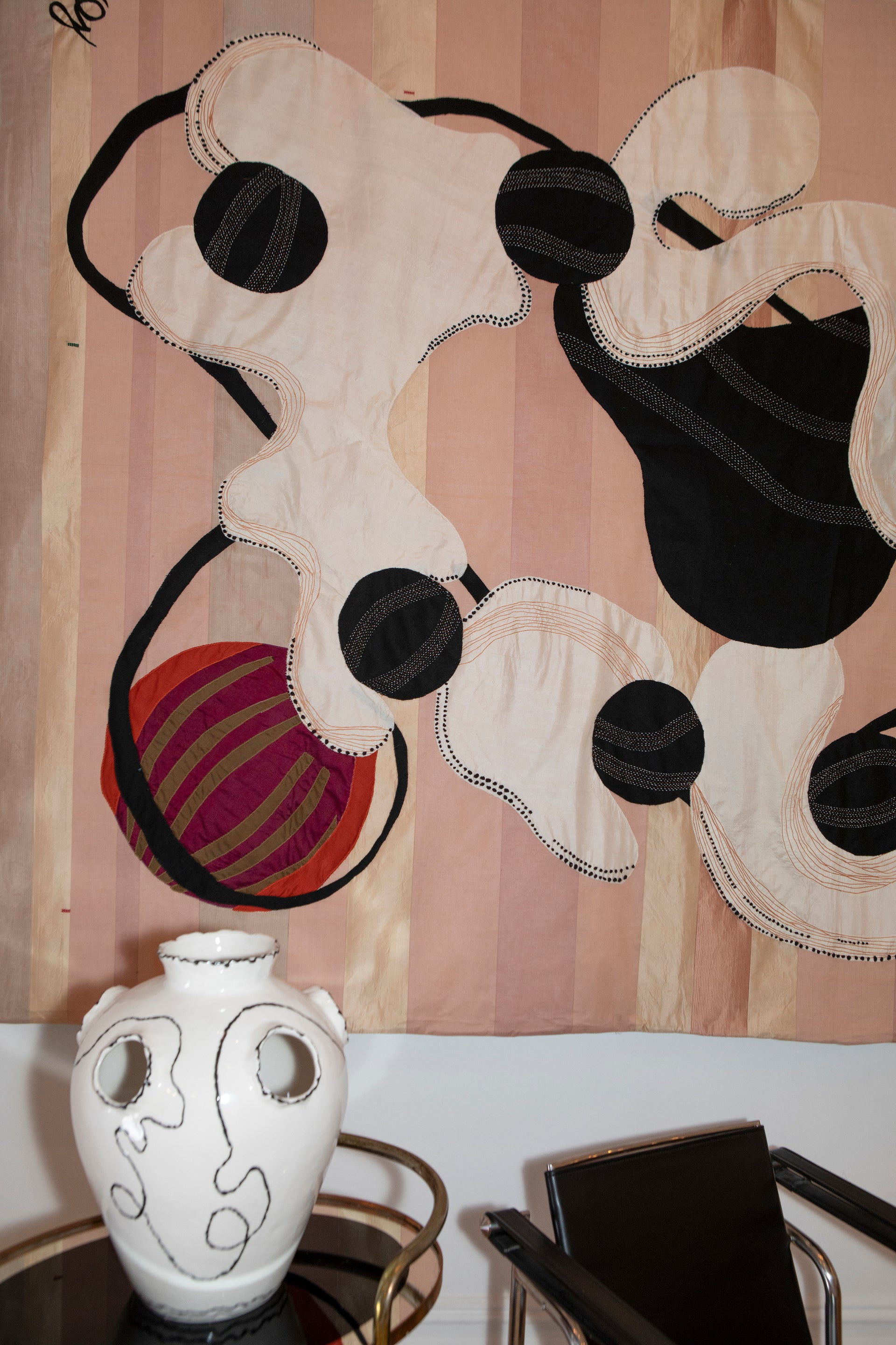 Hand made decorative tapestry with an abstract and surrealist design motif. White and black abstract shapes float on a pink background with an embroidered bird. Hand crafted and hand embroidered from antique silks. Made in India, artisanal home decor. Modern tapestry design. Shown in a home setting with other modernist home decor and furniture. 