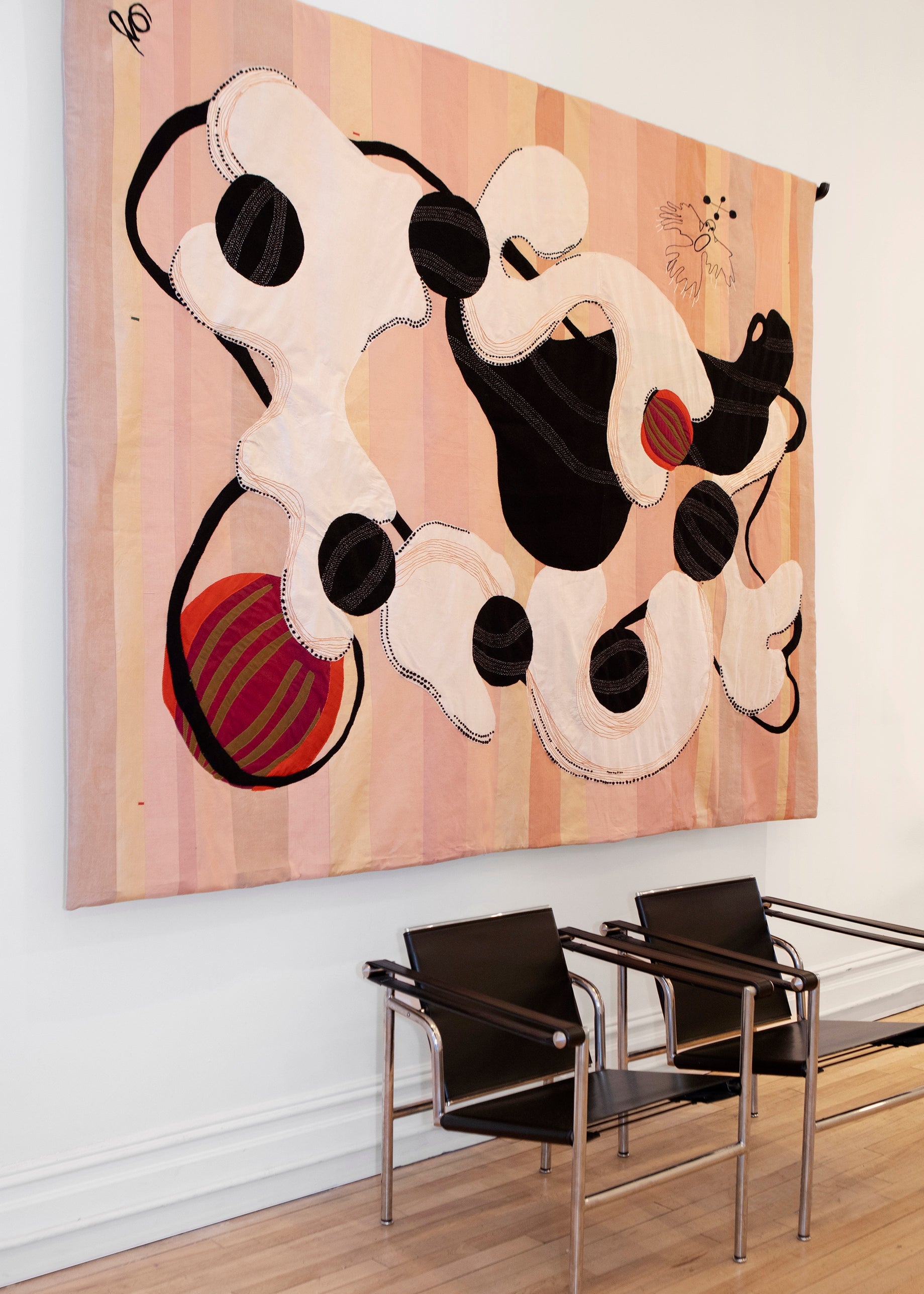 Hand made decorative tapestry with an abstract and surrealist design motif. White and black abstract shapes float on a pink background with an embroidered bird. Hand crafted and hand embroidered from antique silks. Made in India, artisanal home decor. Modern tapestry design. Shown in a home setting with other modernist home decor and furniture. 