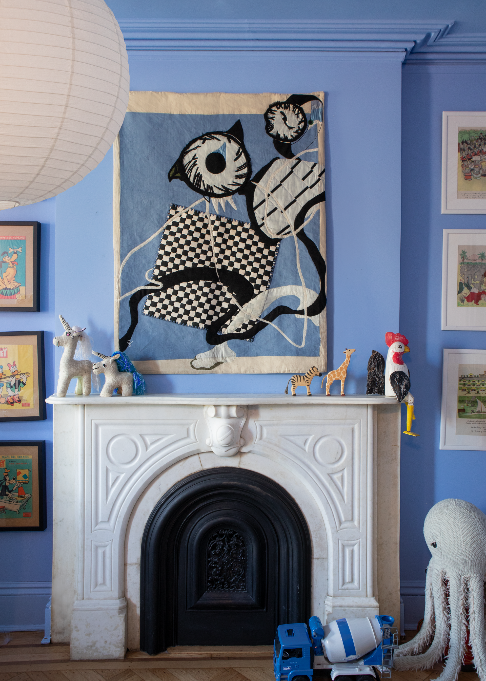 Hand made decorative tapestry with an abstract and surrealist design motif. Features a blue background with a checkerboard design and an abstract eye design. Hand crafted and hand embroidered from antique silks. Made in India, artisanal home decor. Modern tapestry design. Shown in a children's bedroom, styled with other modernist home decor and furniture. 