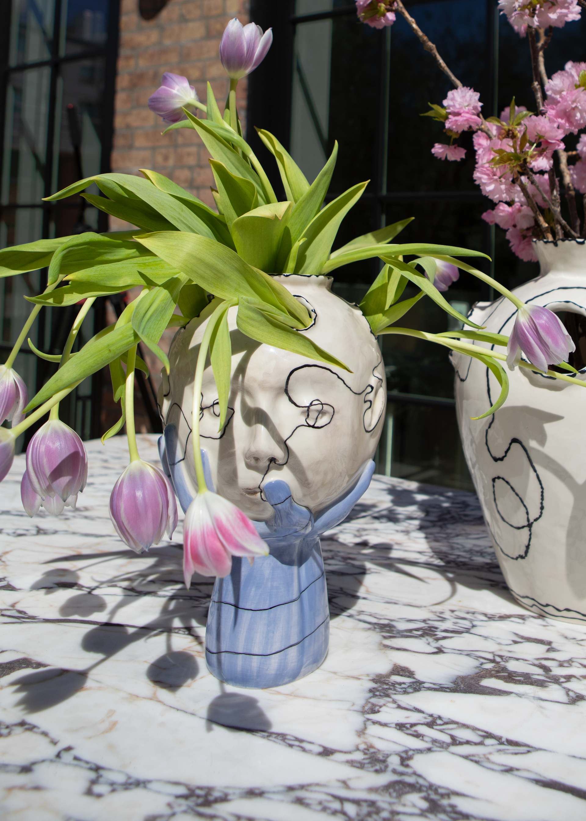 Hand made blue and white ceramic vase with a surrealist face design holding flowers. 