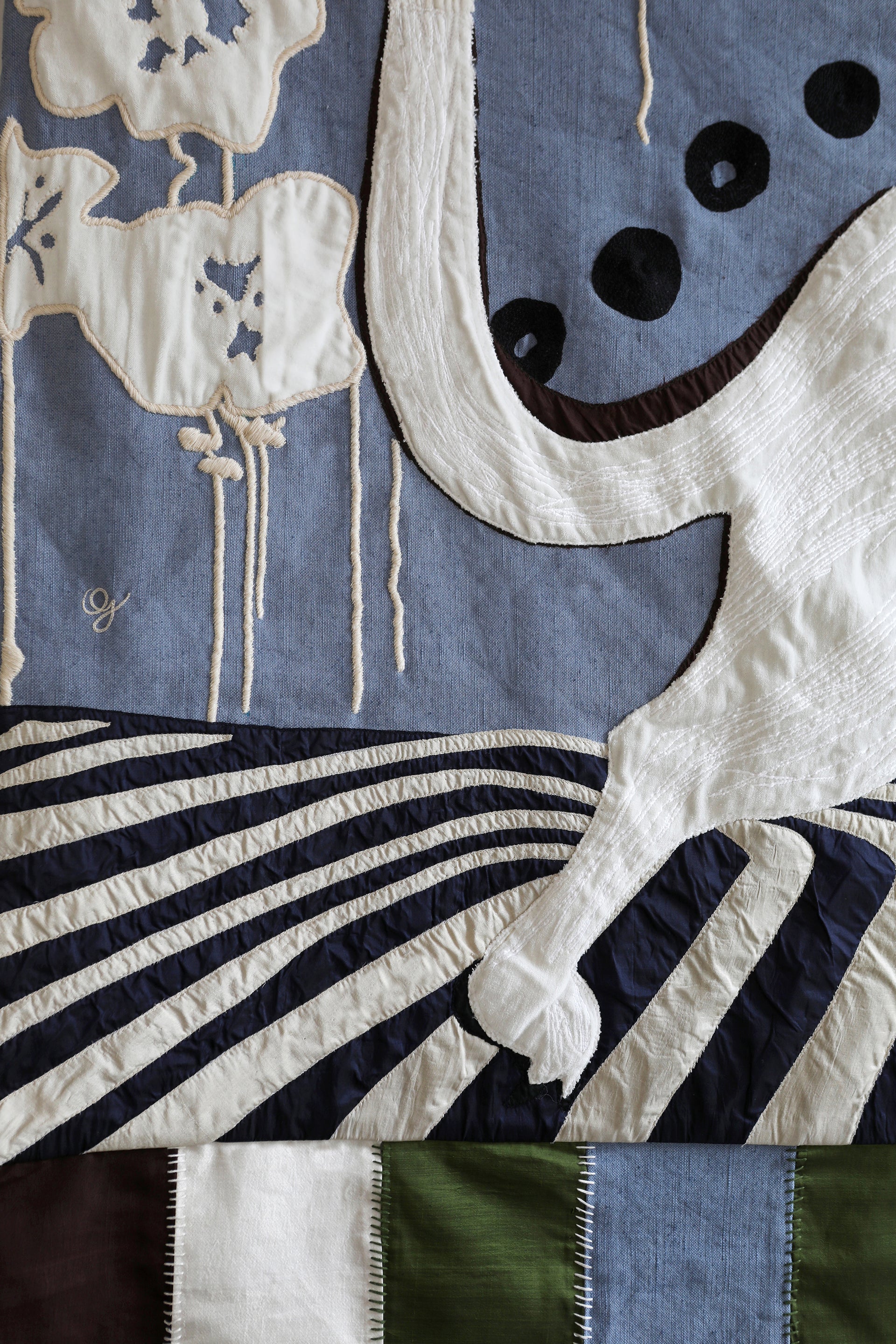 Detail of hand made decorative tapestry with an abstract and surrealist design motif. Features a cat design on a blue background with white flowers and a striped floor. Hand crafted and hand embroidered from antique silks. Made in India, artisanal home decor. Modern patchwork and applique tapestry design. Shown on a wall in a modernist styled home with other abstract home decor. 