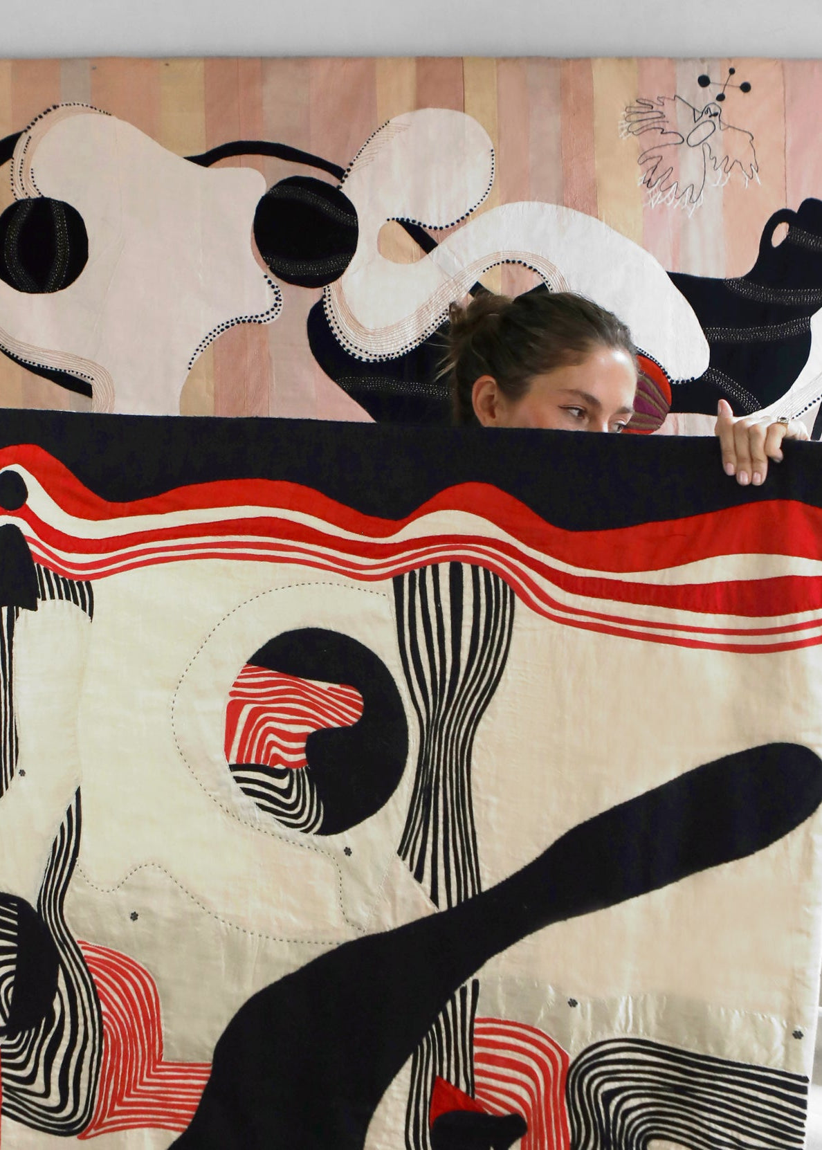 Hand made decorative tapestry with an abstract and surrealist design motif. White and black abstract shapes float on a pink background with an embroidered bird. Hand crafted and hand embroidered from antique silks. Made in India, artisanal home decor. Modern tapestry design. Shown in a home setting with other modernist home decor and furniture. 