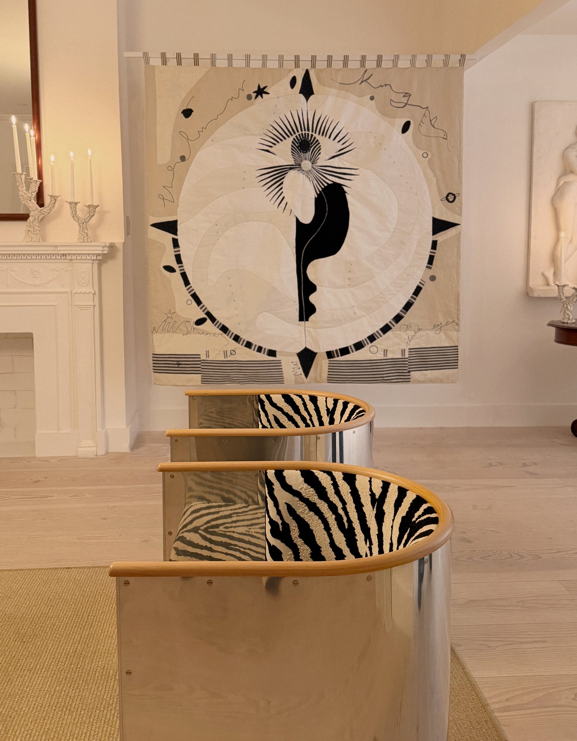 Hand made large decorative tapestry with an abstract and surrealist design motif. A moon design with radiating stars and celestial patterns and line work in an ivory and cream palette. Hand crafted and hand embroidered from antique silks. Made in India, artisanal home decor. Modern tapestry design. Shown in a home setting with modernist home decor and furniture. 