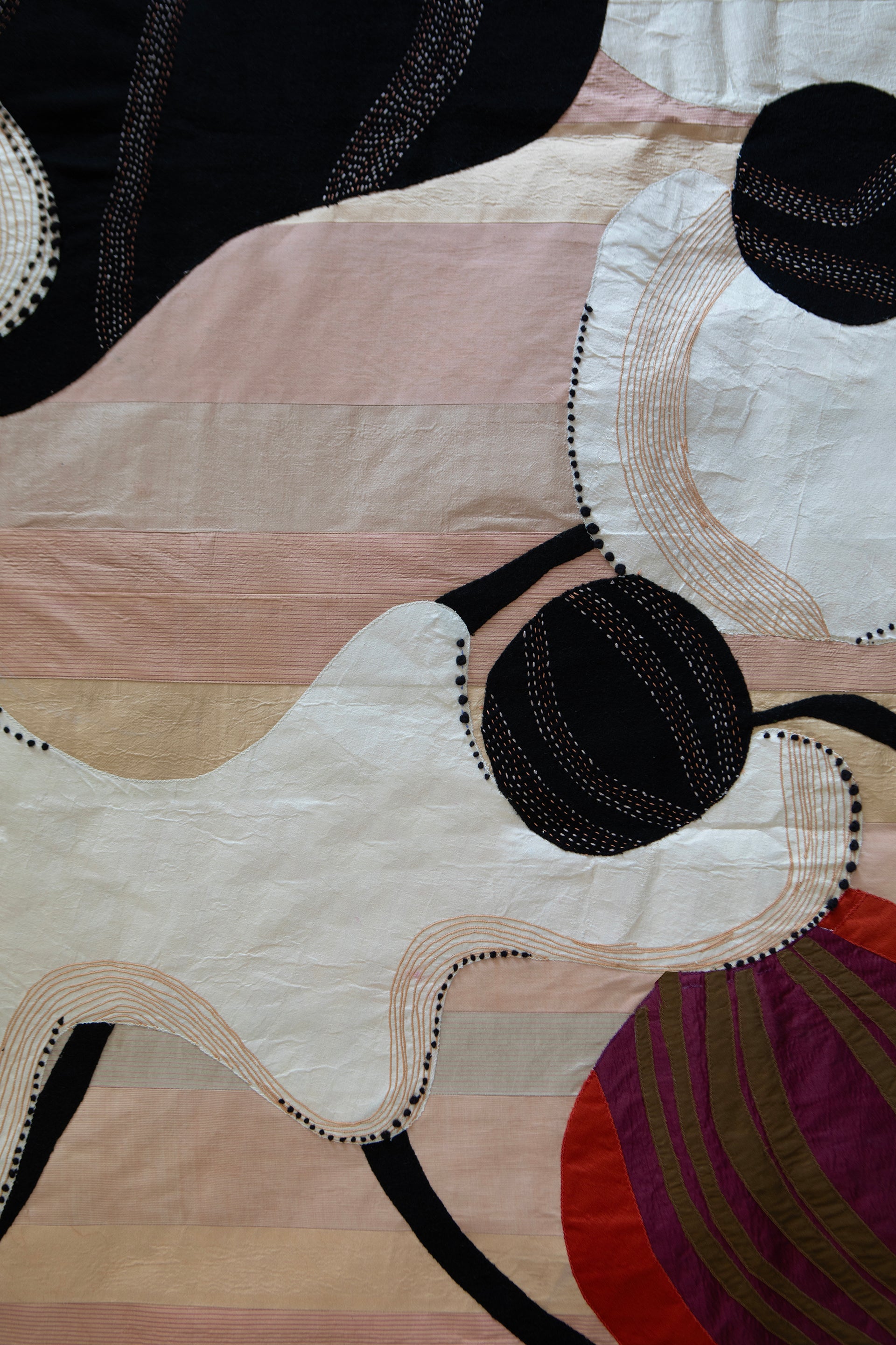 Detail of hand made decorative tapestry with an abstract and surrealist design motif. White and black abstract shapes float on a pink background with an embroidered bird. Hand crafted and hand embroidered from antique silks. Made in India, artisanal home decor. Modern tapestry design. Detail photo shows hand stitching and embroidery.