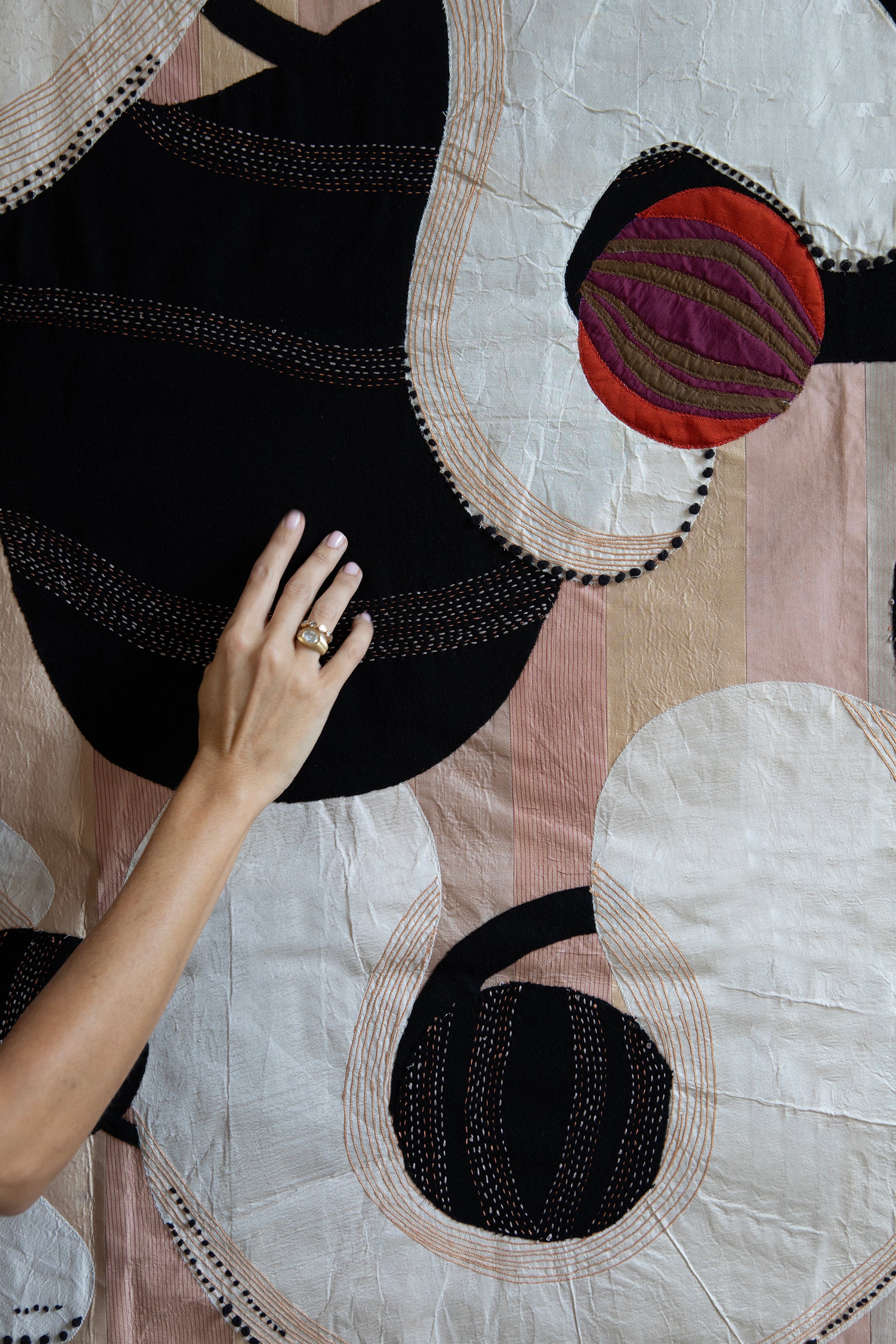 Detail of hand made decorative tapestry with an abstract and surrealist design motif. White and black abstract shapes float on a pink background with an embroidered bird. Hand crafted and hand embroidered from antique silks. Made in India, artisanal home decor. Modern tapestry design. Shown in a home setting with other modernist home decor and furniture. 