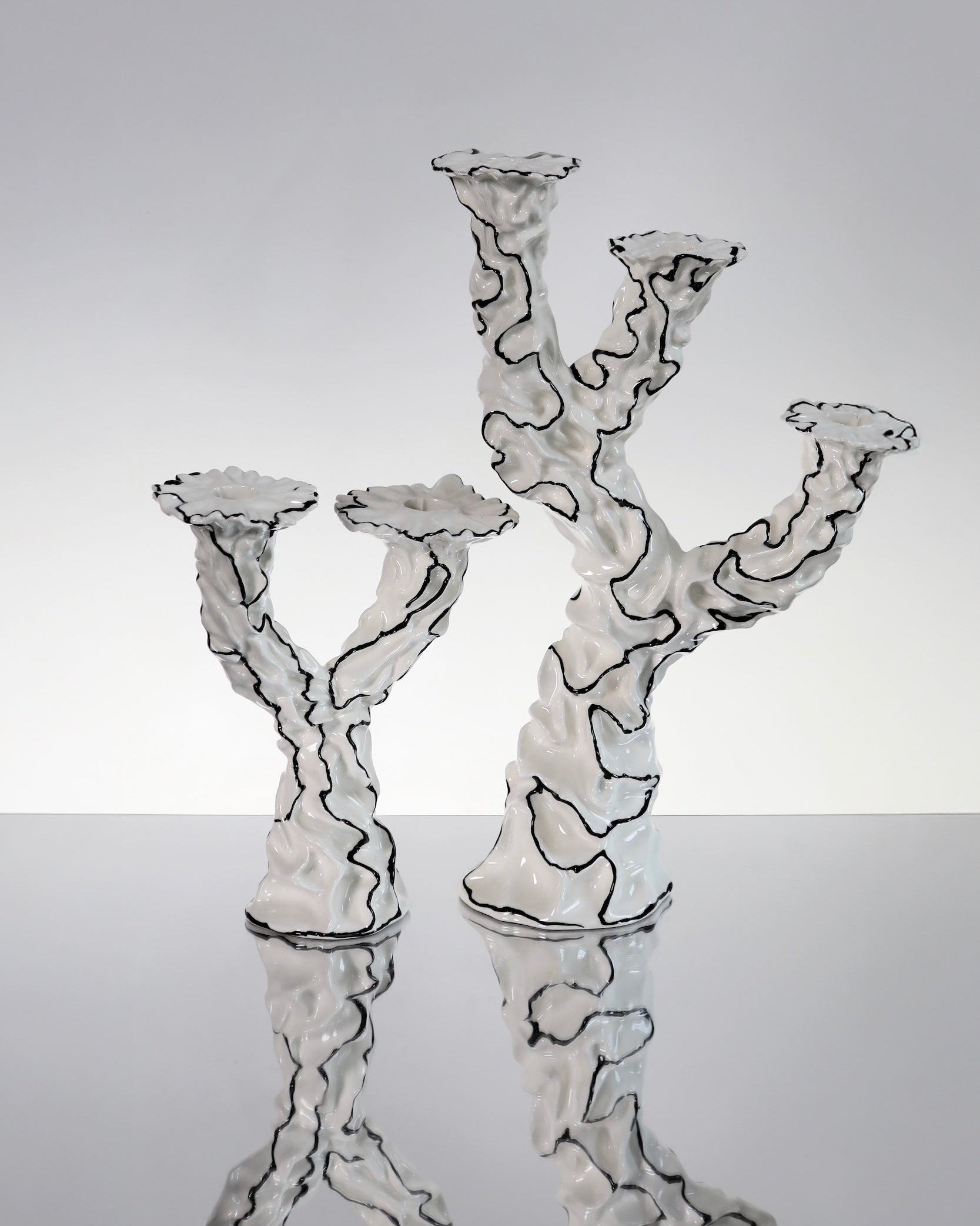 Two hand made sculptural ceramic candle holders with a glossy white glaze and black decorative surrealist, modern line work across the surface. 