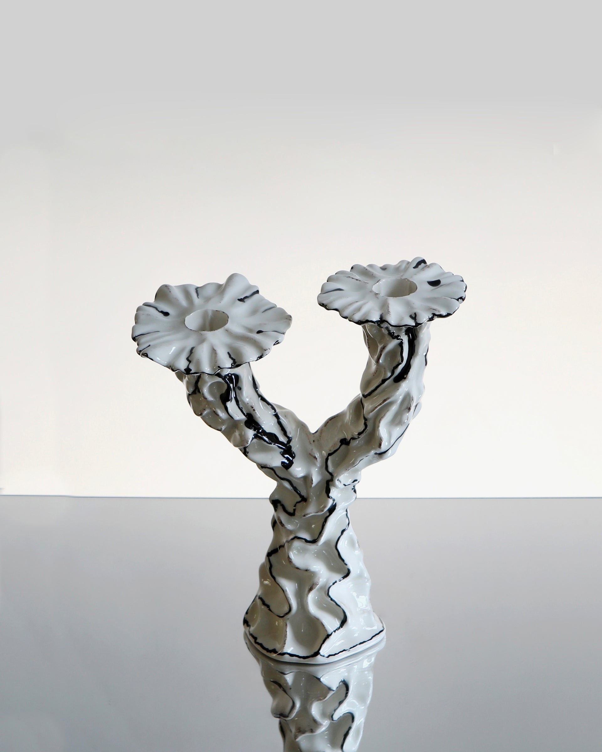 Hand made sculptural ceramic candle holder with two pedestals, shown in a white glossy glaze with black surrealist abstract line work across the surface. 